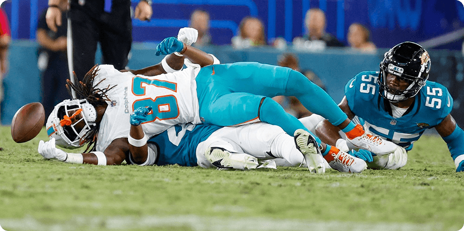 NFL game action — Dolphins and Jaguars player on the field with a loose football, illustrating physical play and injury risk